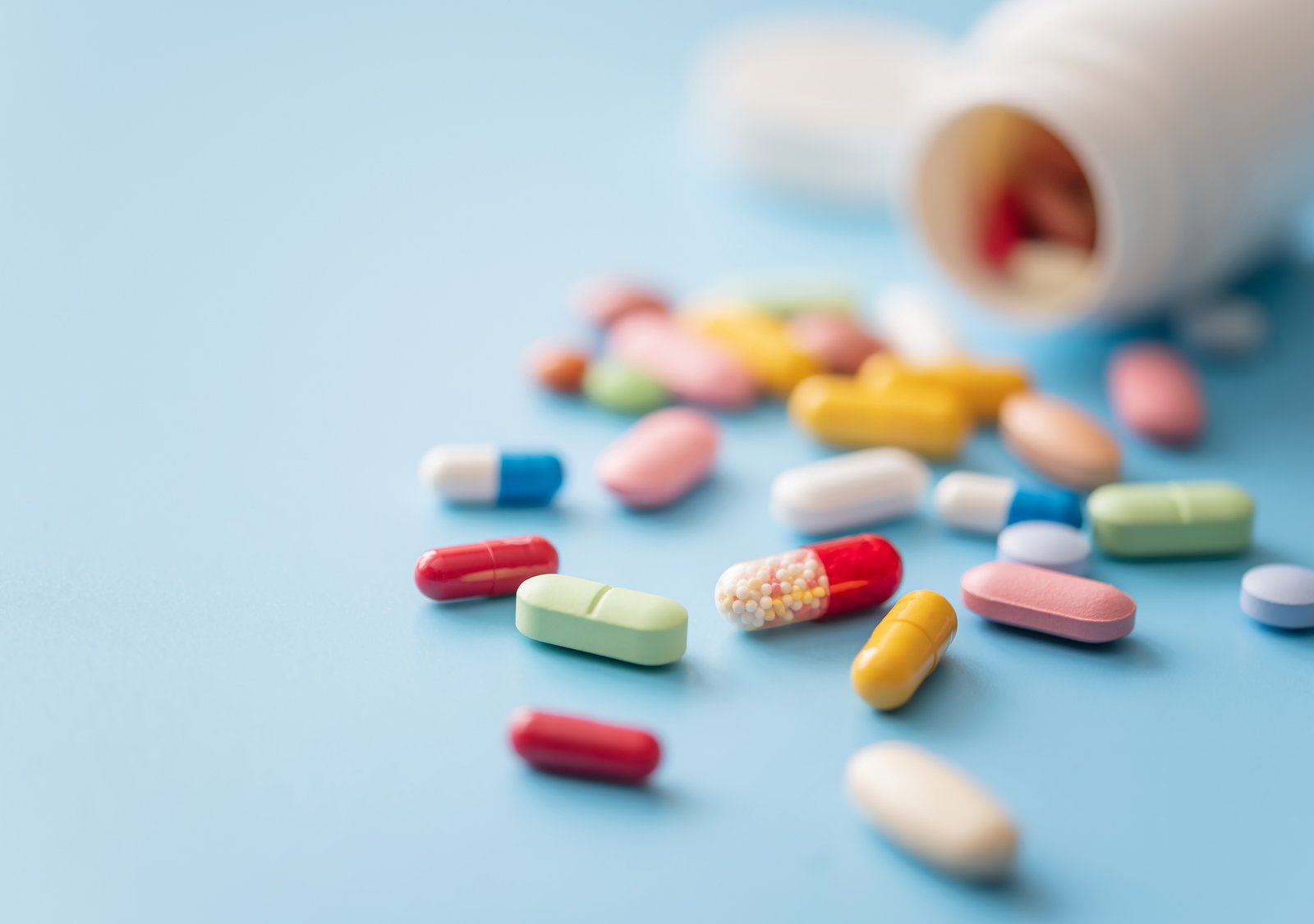 multicolored pills scattered from white plastic medicine container